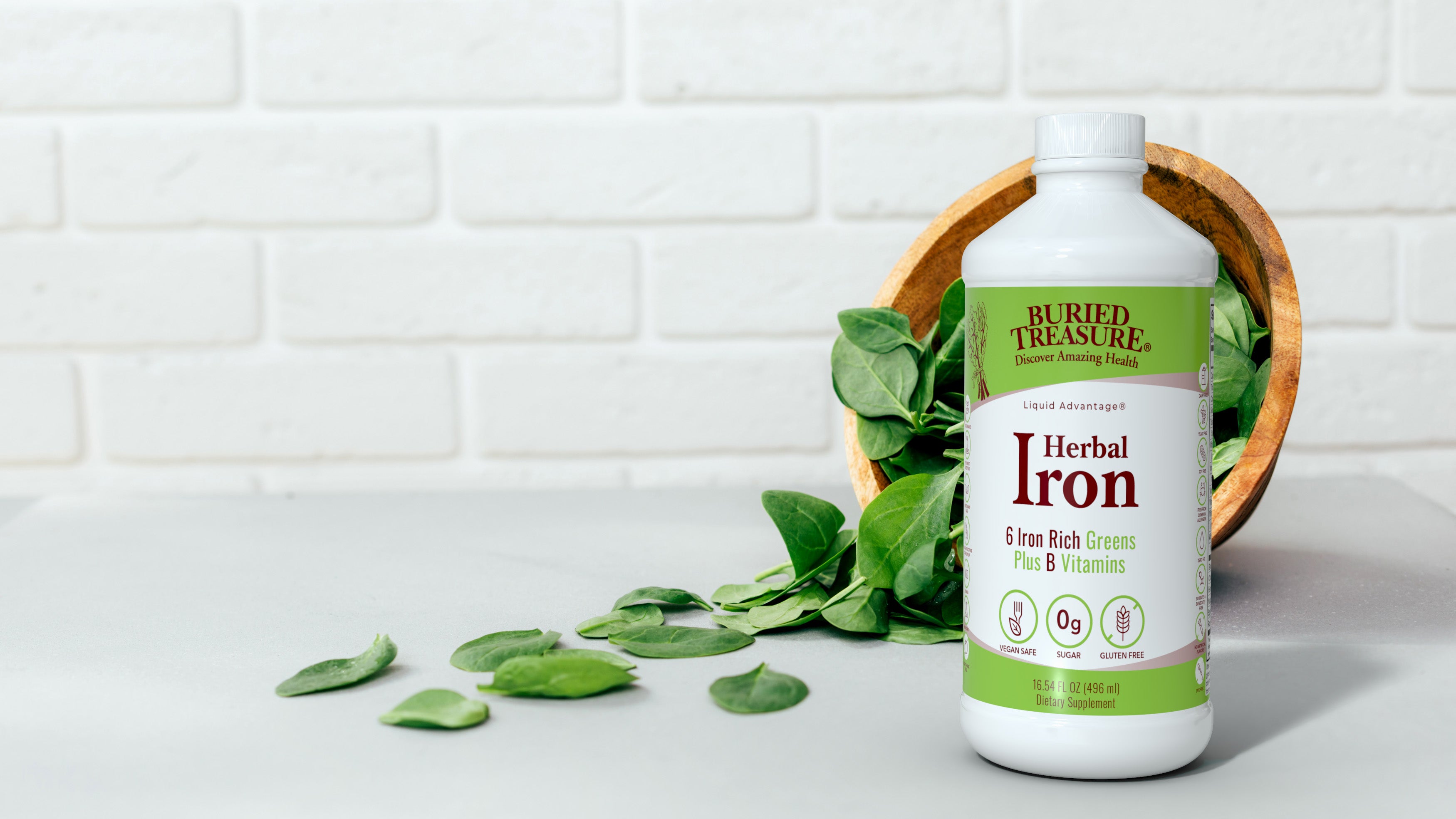Buried Treasure Herbal Iron bottle—liquid iron supplement—surrounded by spinach spilling from bowl; vegan iron supplement.”