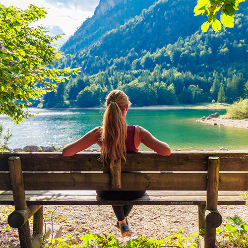 Woman on bench looking across lake, back to camera, represents happy Herbal Iron customer reviewer