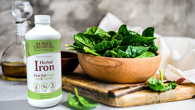 Buried Treasure Herbal Iron vegan liquid iron supplement bottle next to bowl of fresh spinach leaves